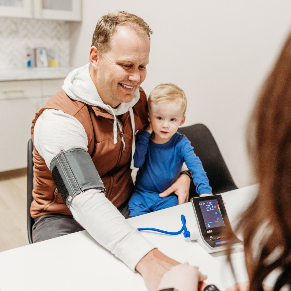 Father and young boy during a post-concussion evaluation at Transcend Headache Clinic, with the father’s blood pressure being checked.