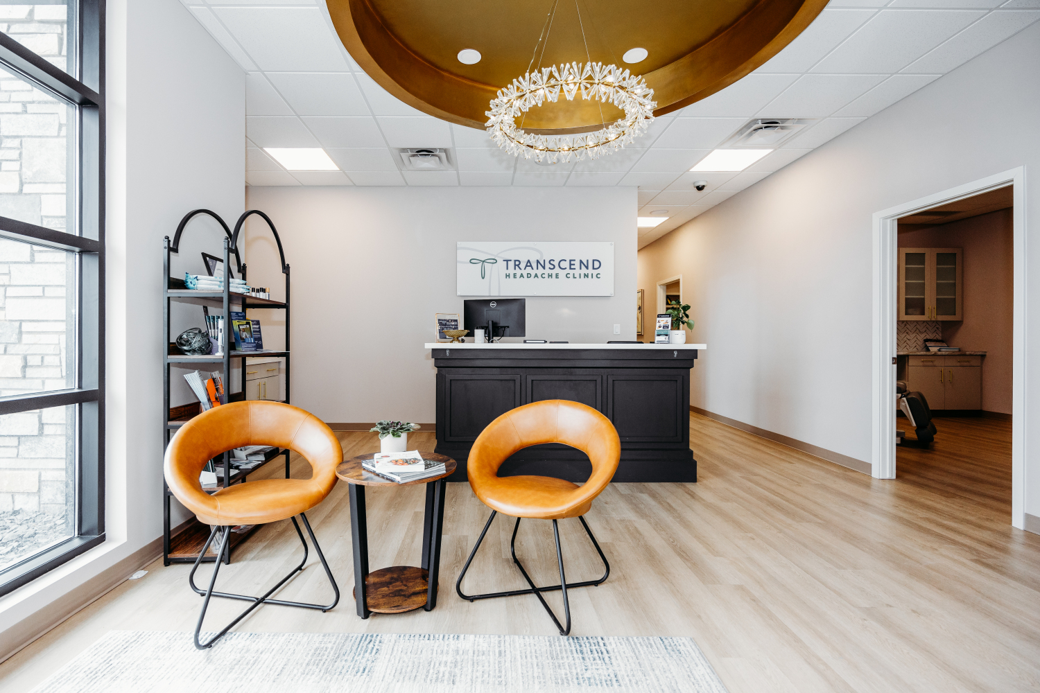 Front desk and waiting area of Transcend Headache Clinic, featuring warm-toned chairs, a chandelier, and clinic signage.