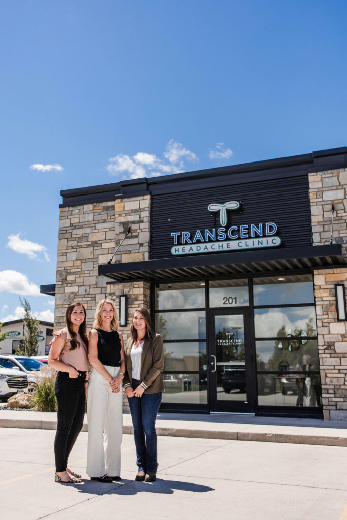 The Transcend Headache Clinic team — Tasha, Tiffany, and Kyrie — stand together outside their West Fargo, ND clinic on a sunny day.
